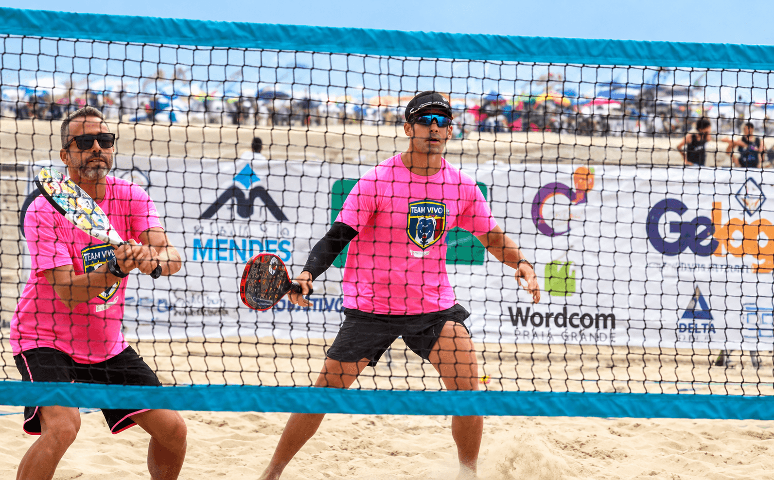 Dupla de atletas com raquetes em uma partida de Beach Tennis.