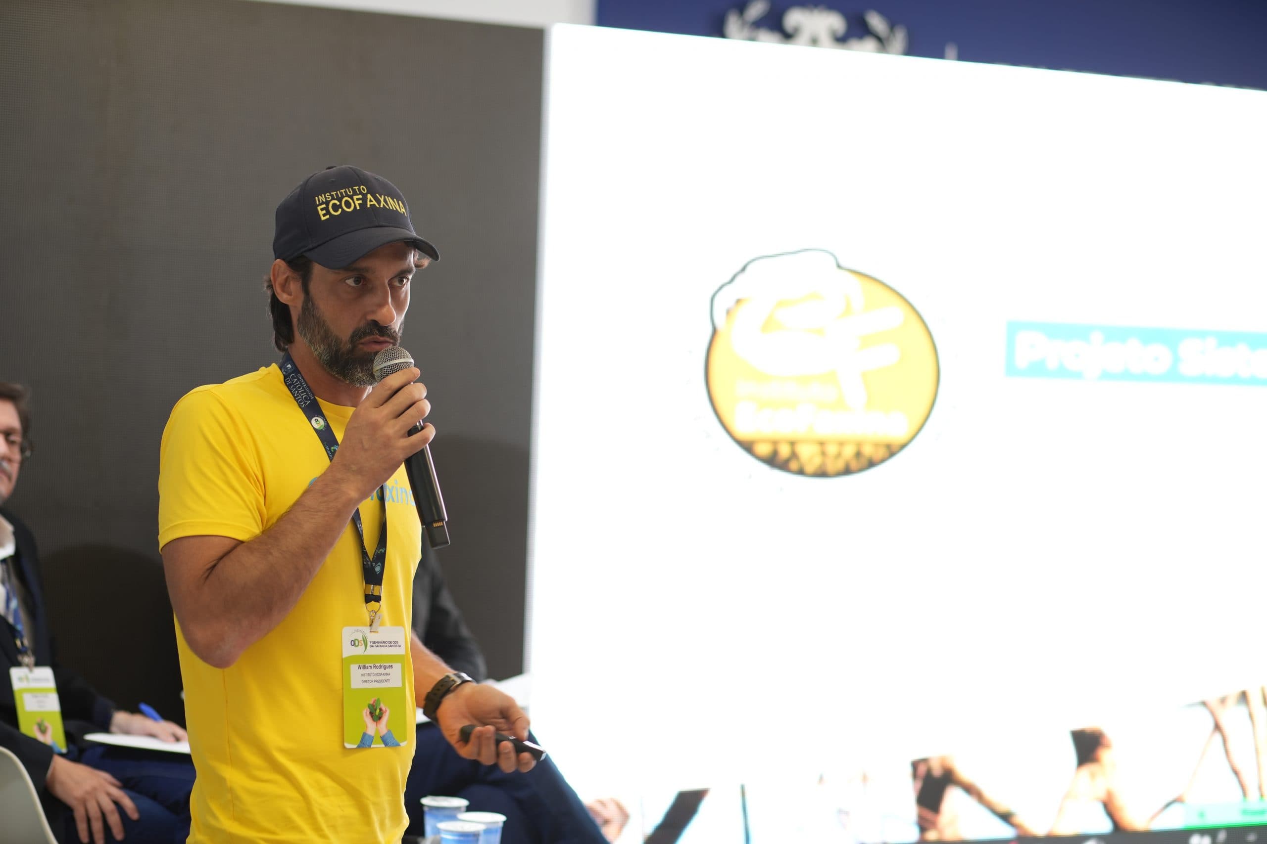 Palestrante de camiseta amarela apresentando com microfone